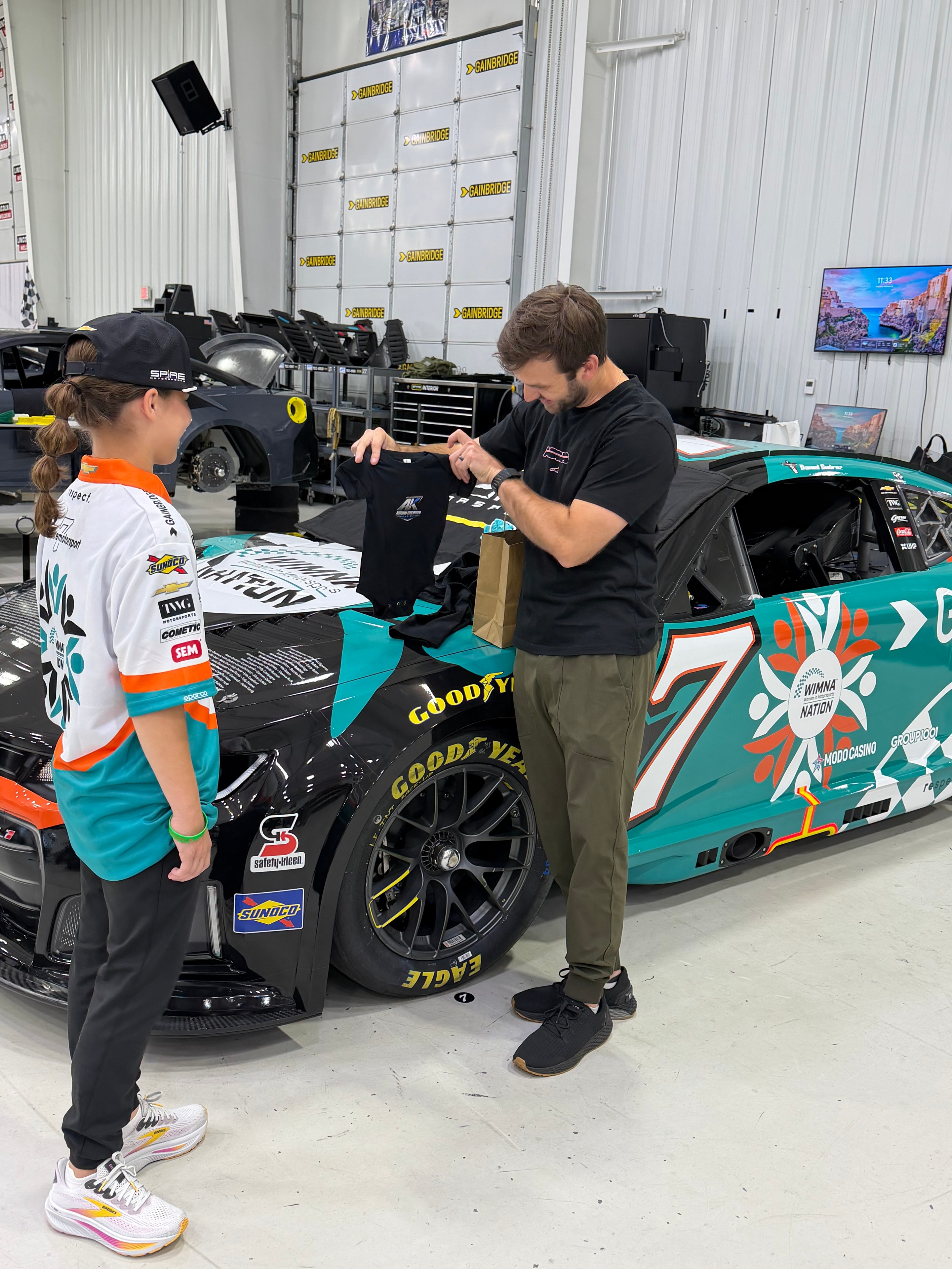 Autumn gifts Daniel Suárez a custom baby onesie with her race logo at Spire Motorsports headquarters